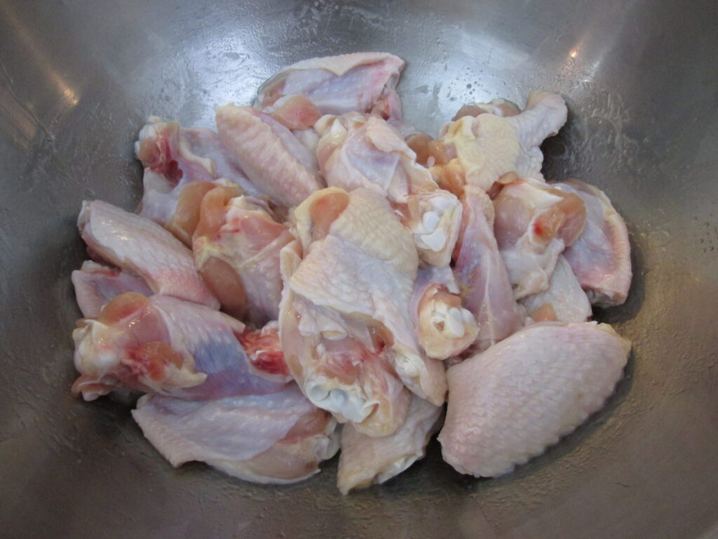 Raw chicken wings being prepared to be seasoned with flour in a bowl.