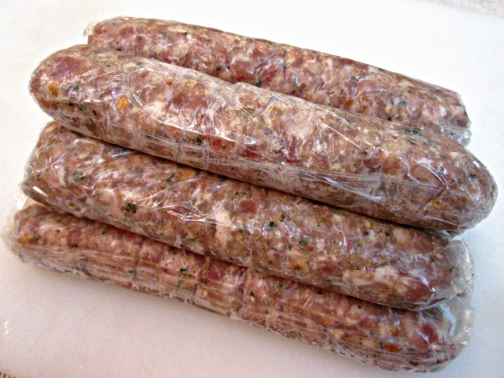 Raw Italian sausage links wrapped in plastic wrap, stacked and prepared for storage or cooking