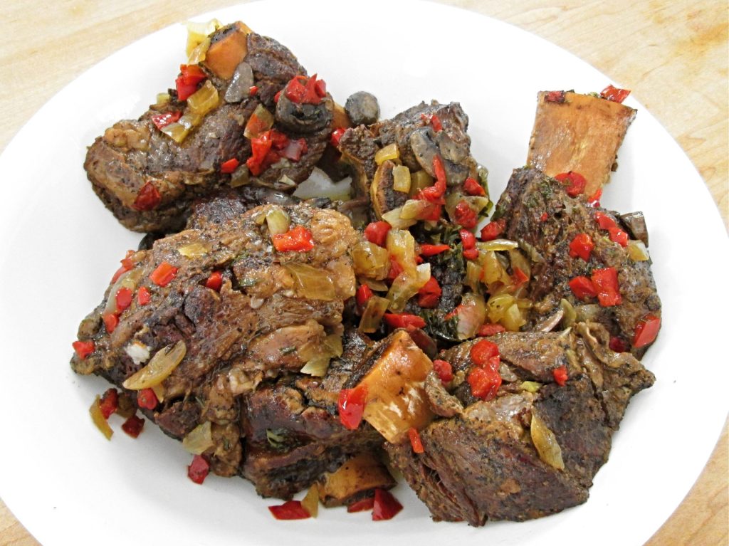 Close-up of tender beef short ribs covered with cooked mushrooms, onions and diced sweet pappers.