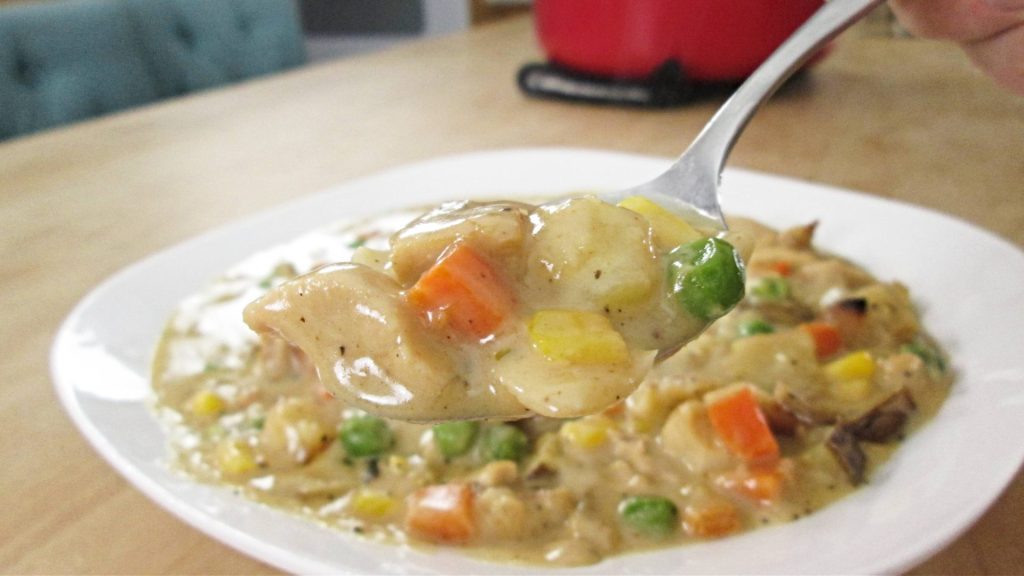 Serving a large bowl and spoon full of corn chowder with chicken.