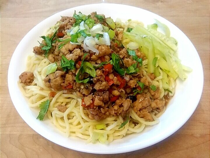 Chicken Dan Dan Noodles served with sliced cucumber, topped with scallions and chopped cilantro.