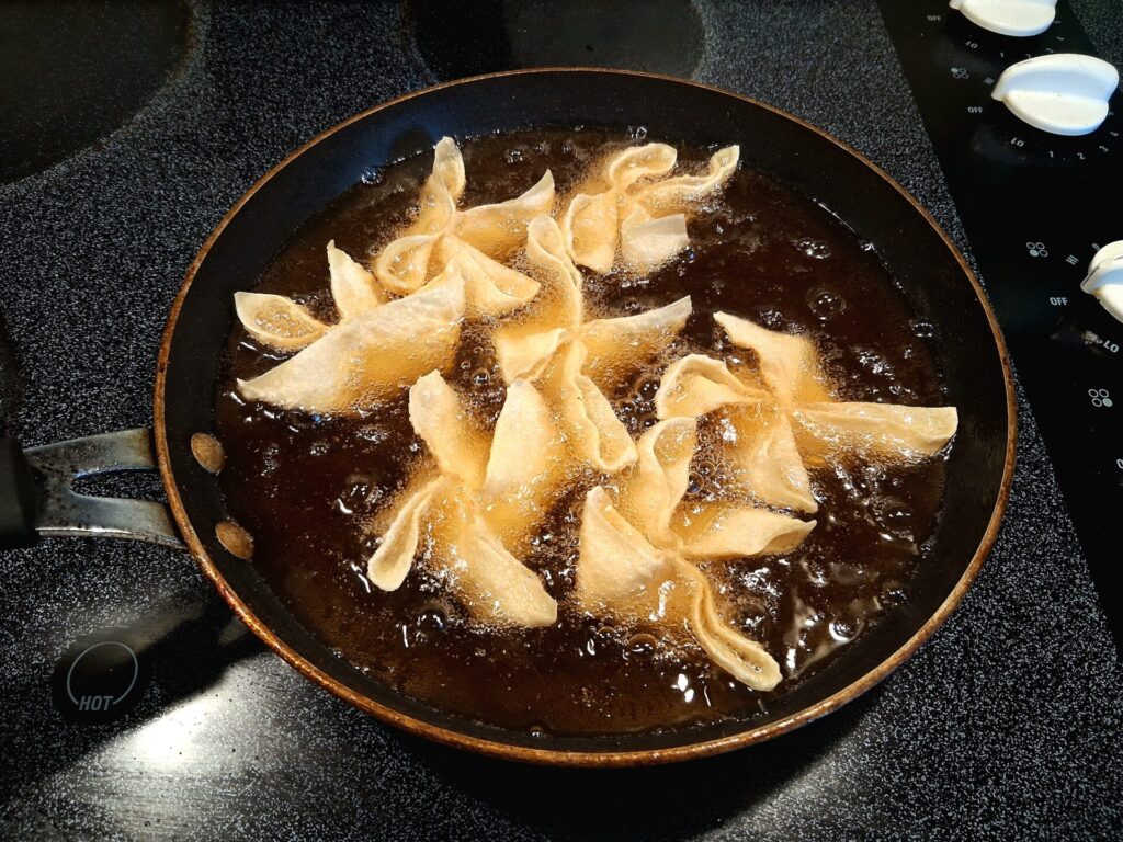 Crab Rangoon frying in hot oil until golden brown.
